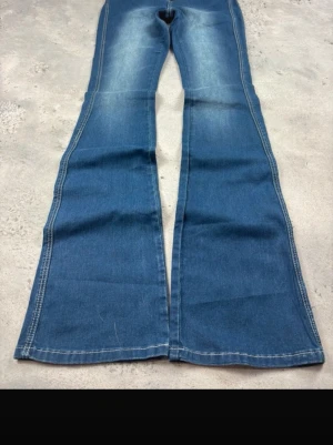 Blå utsvängda jeans med vintagekänsla - Säljer ett par blå jeans med utsvängda ben och markerade sömmar. Jeansen har en klassisk femficksmodell och en snygg tvätt med ljusare partier framtill. Perfekta för dig som gillar retrostil och vill sticka ut med en cool siluett.