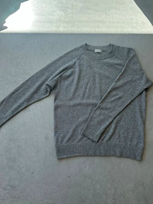 Grå stickad tröja från Filippa K - Snygg grå stickad tröja från Filippa K med rund halsringning och ribbade muddar vid ärmslut och nederkant. Tröjan har en enkel och stilren design som passar perfekt till olika outfits. Mindre än L i storlek, skulle uppskatta M. 100% cashmire 