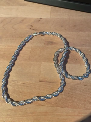 Tjockt tvinnat halsband i silverfärg - Säljer ett snyggt halsband i 925 silverfärg med tvinnad design. Kedjan är rejäl och har en blank finish som fångar ljuset. Perfekt för dig som gillar statement-smycken och vill ha något som sticker ut. Lås med karbinhake för extra säkerhet. 8mm bred och 60cm lång