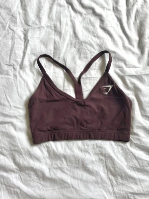 Plommon sport-bh från Gymshark - Snygg plommon sport-bh från Gymshark med smala axelband och brottarrygg. Tillverkad i ett stretchigt och mjukt material som ger bra stöd. Perfekt för träning. Storlek XS🤍80kr