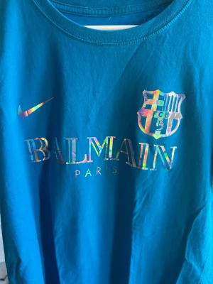 Blå Balmain x Nike FC Barcelona T-shirt - Snygg blå t-shirt med Balmain Paris-tryck och FC Barcelona. Yamal på ryggen. Balmain trycket åker av och man behöver strycka på de ibland men Yamal trycket är av svin bra kvalité