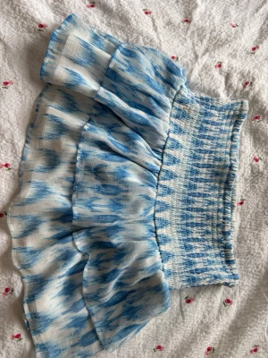 Blåvit volangkjol från Gina Tricot - Supersöt kort kjol från Gina Tricot i blått och vitt med volanger och smock i midjan. Kjolen har ett unikt mönster och är perfekt för sommarens alla tillfällen. Tillverkad i ett lätt och luftigt material som känns skönt mot huden. Såklart tvättas den innan jag skickar iväg den