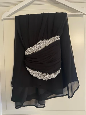 Svart axelbandslös kortklänning med pärlor - Snygg svart axelbandslös kortklänning med pärlor längs bysten. 