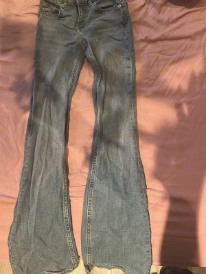Blå utsvängda jeans med hög midja - Säljer ett par blå jeans med utsvängda ben och hög midja. Klassisk femficksmodell med dragkedja och knapp framtill. Jeansen har en snygg tvättad look och är tillverkade i denim. Perfekta för dig som gillar retrostil och vill sticka ut.