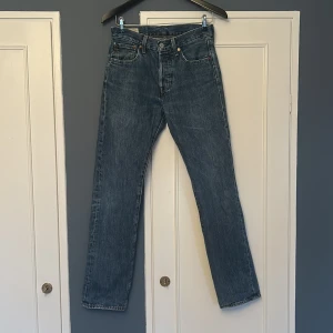 Levi's 501 blå jeans - Klassiska blå jeans från Levi's med rak passform. Jeansen har en tidlös tvätt och är tillverkade i slitstark denim. Perfekta för en avslappnad och stilren look. Stängs med knappgylf och har Levi's ikoniska läderpatch bak. Nypris 1100-1200 kr. Strl W28 L32.