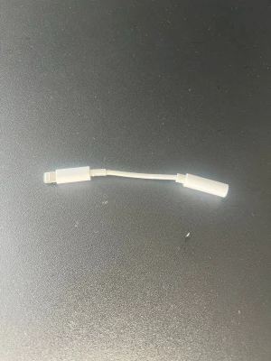 Lightning till 3.5mm adapter Apple - Vit adapter från Apple som omvandlar Lightning-kontakt till 3.5mm hörlursuttag. Perfekt för att koppla in vanliga hörlurar till din iPhone. Smidig och kompakt design i plast som är enkel att ta med sig överallt.
