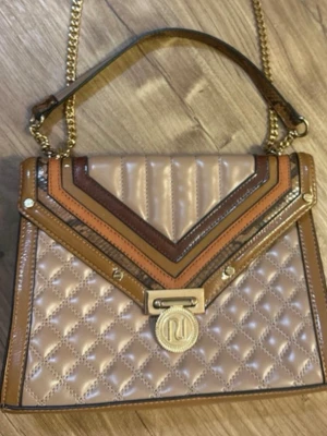 Beige quiltad axelväska från River Island - Snygg beige axelväska från River Island med quiltat mönster och detaljer i brunt, guld och orange. Väskan har guldfärgad kedjerem och ett stort RI-emblem framtill. Materialet är glansigt konstläder och väskan har en cool geometrisk design på locket.