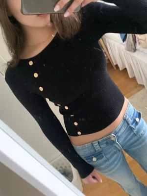 Svart ribbad topp med knappar - Jättesnygg svart tight långärmad tröja med guld ”knappar” som detalj. Använd fåtal gånger!