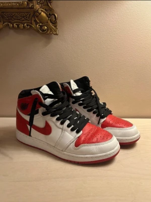 Nike Air Jordan 1 Chicago High - Säljer ett par klassiska Nike Air Jordan 1 Chicago High sneakers i vitt, rött och svart läder. Skorna har svarta skosnören, perforerad tåbox och swoosh-loggan.
