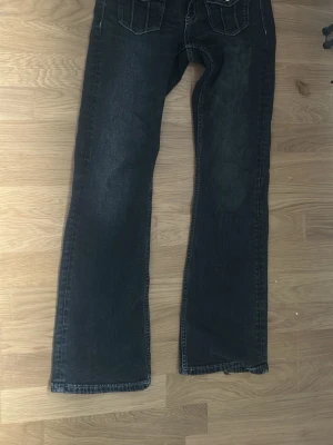 Svarta bootcut jeans med fickor - Säljer ett par svarta bootcut jeans med två  bakfickor och kontrastsömmar. Jeansen har en klassisk femficksmodell och är tillverkade i denim. Perfekta för dig som gillar en avslappnad men ändå snygg stil.