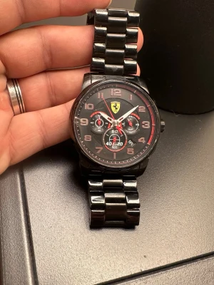 Svart Ferrari klocka stainless still  - Snygg svart klocka från Ferrari med metallarmband och sportig design. Urtavlan är svart med röda detaljer, tre subdials och Ferraris klassiska logga högst upp. Siffrorna är tydliga och armbandet är robust i metall för en cool look.