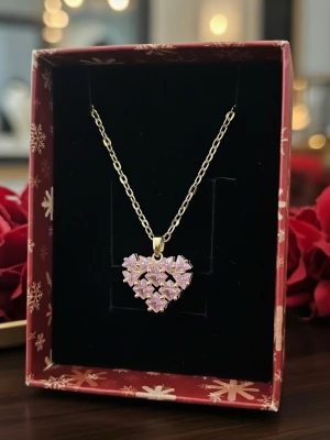 Halsband med hjärthänge och rosa stenar - Guldigt halsband med ett hjärtformat hänge dekorerat med flera små, ljusrosa stenar som ger ett glittrande intryck. Kedjan är tunn och elegant, och hänget har en modern, ungdomlig design. Perfekt accessoar för att lyfta vilken outfit som helst.