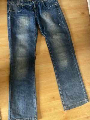 Blå raka jeans med slitningar - Säljer ett par blå jeans med raka ben och snygga slitningar på låren och knäna. Jeansen har klassisk femficksdesign och en något lösare passform. Knappt använda 😊midjemått: 39 inerbenslängd:84