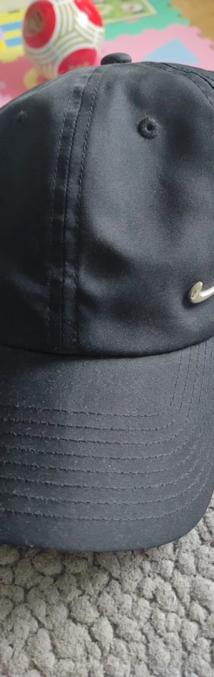 Svart Nike keps Heritage86 - Snygg svart keps från Nike, modell Heritage86. Klassisk böjd skärm och justerbar passform. Tillverkad i slitstarkt tyg med diskret Nike-logga på insidan. Perfekt för en sportig och avslappnad stil.