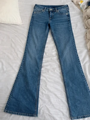 Blå bootcut jeans med fickor - Säljer ett par klassiska blå bootcut jeans med fem fickor och snygga sömmar. Jeansen har utsvängda ben och normal midja, perfekta för en retroinspirerad look. Tillverkade i denim med knapp- och dragkedjestängning framtill.