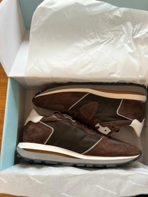OANVÄNDA Philippe Model 44 - Snygga sneakers från Philippe Model i mörkbrun mocka och mesh med vita detaljer och svart yttersula, perfekta inför våren. Skorna har aldrig haft en fot i sig, aldrig klivit ett steg, sprillans nya som ni kan se på den andra bilden. De är självklart äkta och kvitto ingår. Antingen kan ni hämta dem i sollentuna eller så kan jag frakta de genom plick. Storleken är 44, nypris ligger på 3500kr, mitt pris endast 2099kr.