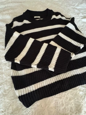 Svartvit randig stickad tröja/ JDY - Stickad tröja från JDY i svart och vitt med svartvita ränder. Tröjan har rund halsringning och långa ärmar. Grovstickad struktur som ger en avslappnad och trendig look. Perfekt för lager på lager under kyliga dagar.