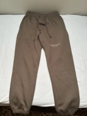 Bruna mjukisbyxor från essentials  - Säljer ett par bruna mjukisbyxor från essentials med dragsko i midjan och resår vid bensluten. Byxorna har tryckt logga på vänster lår och en bakficka. Perfekta för chill dagar och riktigt sköna att ha på sig. Strlk M men passar S