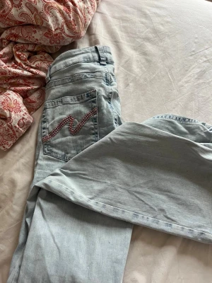 Ljusblå bootcut jeans från Nelly - Säljer ett par ljusblå bootcut jeans från Nelly med snygg rosa zigzag-detalj på bakfickan. Jeansen har klassisk femficksdesign, normal midja och är gjorda i mjuk denim. Perfekta för dig som gillar en avslappnad men trendig look.