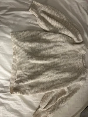 Beige oversized stickad tröja - Mysig beige stickad tröja med breda ärmar och ribbade muddar. Tröjan har en avslappnad, oversized passform och är gjord i ett mjukt, tjockt material som passar perfekt för kyligare dagar. Rund halsringning och diskret ribbad struktur över hela plagget.