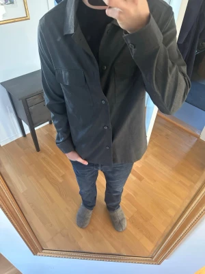 Mörkgrå overshirt med fickor - Stilren mörkgrå overshirt med knäppning framtill och två bröstfickor. Rak passform och klassisk krage, perfekt att bära över en t-shirt.  Använd 1 gång.