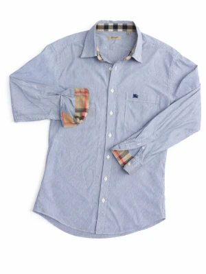 Blårandig skjorta från Burberry - Klassisk blårandig skjorta från Burberry med ikoniskt rutigt tyg på insidan av krage och manschetter. Skjortan har lång ärm, bröstficka med broderad logga och vita knappar framtill. Perfekt för en stilren och tidlös look.