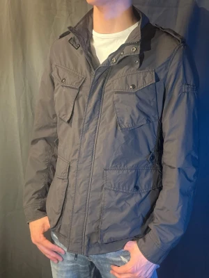 Woolrich Field Jacket - Säljer en mörkgrå Field jacket från woolrich perfekt nu till våren. Modellen är 190cm och väger 80kg. Skriv om du har fler frågor 🥰