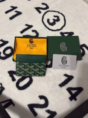 Grön korthållare från Goyard - Snygg grön korthållare från Goyard med det klassiska vita och gröna mönstret. Tillverkad i canvas och läder, perfekt för kort och ID. Kommer med originalask och certifikat. En riktigt lyxig accessoar för dig som gillar exklusiva detaljer.