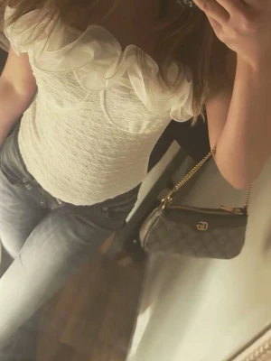 Vit volangprydd korsettopp - Supersnygg vit korsettopp med volangdetaljer längs urringningen. Toppen är figurnära och har en romantisk vibe, perfekt att styla med jeans eller kjol. Materialet känns mjukt och lätt, och toppen är ärmlös för en fräsch look.