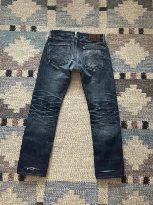 RRL selvage jeans 29/30 - Ett par low-rise RRL Selvedge jeans med sjuk patina! Storlek 29/30 (se mått nedan). Bra skick, har blivit lagade i grenen och slitningar över båda benöppningarna. Skriv om du har frågor! Mått: Storlek på tag - 29/30, Midja - 40.5 cm, Lår - 28.5 cm, Innersöm - 78.5 cm, Längd - 99 cm, Benöppning - 19 cm