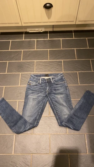 Blå slim fit jeans från tiger of sweden  - Snygga blå slim fit jeans från tiger of sweden med klassisk femficksmodell och diskreta slitningar. Jeansen har normal midja, dragkedjegylf och är tillverkade i stretchigt denim för extra komfort. Perfekta till en avslappnad streetstyle-look.