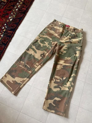 Supreme Camo Carpenter pants - Säljer ett par cargobyxor från Supreme i klassiskt camomönster. Byxorna har raka ben, flera stora fickor på sidorna och bak, samt robust bomullsmaterial.