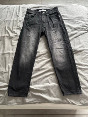 Svarta raka jeans med slitningar - Snygga svarta jeans med raka ben och diskreta slitningar framtill. Klassisk femficksmodell med knapp och dragkedja. Jeansen har en cool tvättad look och passar perfekt till en avslappnad stil. Litet märke vid ena bakfickan som knappt är synbart.