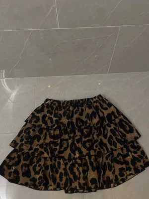 Leopardmönstrad volangkjol - Säljer en kort kjol med leopardmönster och flera volanger. Kjolen har elastisk midja.