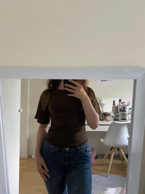 Brun t-shirt  - Säljer en brun t-shirt med korta ärmar och rund halsringning. T-shirten har en snygg snörningsdetalj i sidan som ger en cool och trendig look. Perfekt att matcha med jeans eller kjol för en avslappnad stil.