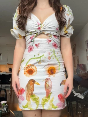 Vit kortklänning med blommor och fåglar - Supersöt kortklänning som är perfekt till midsommar den har en dragkedja i sidan och är stretchig i ryggen 💓
