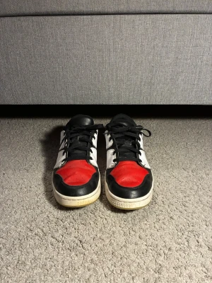 Nike Jordan golfskor - Säljer ett par snygga Golfskor med svart, vitt och rött läder. Skorna har låga skaft, svarta skosnören och en vit sula. Perfekta för dig som gillar sportig stil och vill sticka ut lite extra. Märket syns på sidan av skon. Storlek 44