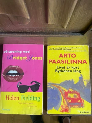 Bridget Jones & Livet är kort Rytkönen lång - Två skönlitterära pocketböcker: 'På spaning med Bridget Jones' av Helen Fielding med rosa och gul framsida, samt 'Livet är kort Rytkönen lång' av Arto Paasilinna med gul och blå framsida. Perfekta för dig som gillar humor och underhållande berättelser.