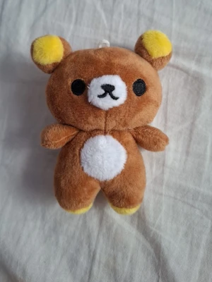 Rillakuma plush  - Söt brun rillakuma plush i form av en nallebjörn med gula detaljer på öronen och tassarna. Den har svart broderad nos och ögon samt en vit mage och nosparti. Perfekt som dekoration eller att ha som nyckelring. Tillverkad i mjukt plyschmaterial.