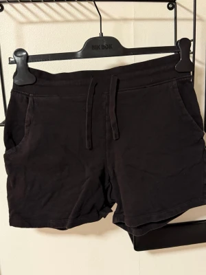 Svarta shorts med snörning från Bik Bok - Svarta mjuka shorts från Bik Bok med snörning i midjan och två sidofickor. De har en relaxed fit och är perfekta för chill dagar. Tillverkade i bomull för en skön känsla.