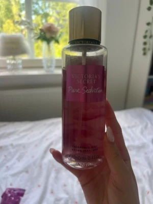 Victoria's Secret Pure Seduction mist - Victoria's Secret Pure Seduction är en body mist i en cylinderformad plastflaska med guldigt lock. Flaskan är transparent med rosa etikett och innehållet är rosa. Doften har inslag av plommon och fresia. Volymen är 250 ml.