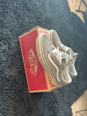 Gråa Vans Old Skool sneakers - Säljer ett par klassiska Vans Old Skool sneakers i grått med vita detaljer och vit sula. Skorna har den ikoniska sidostripen och är tillverkade i mocka och canvas. Perfekta för dig som gillar streetwear och vill ha en tidlös look.