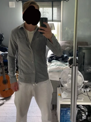 Ljusgrå overshirt  - Säljer en ljusgrå overshirt.Skjortan har klassisk krage, bröstficka med knapp och stängs med stora knappar framtill. Perfekt att bära öppen eller stängd över en t-shirt. Riktigt snygg till sommarn. XS-S, sprillans ny!