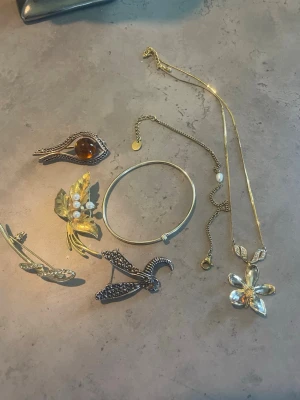 Mix av vintage smycken i guld  - Säljer ett blandat set med vintage smycken: halsband med blomma, armband, broscher  i guld. Några dekorerade med pärlor, bärnsten och gnistrande stenar. Perfekt för dig som gillar unika accessoarer och retrostil.