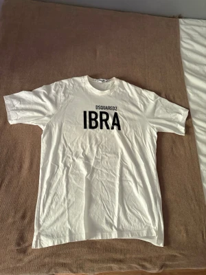 Vit DSQUARED2 IBRA t-shirt - Snygg vit t-shirt från DSQUARED2 med stor svart IBRA-print på bröstet. Klassisk passform med rund hals och korta ärmar. Perfekt för dig som gillar stilrena och trendiga plagg med statement-tryck.