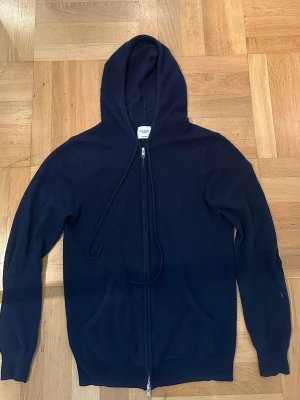 Mörkblå cashmere hoodie John Henric - Mjuk och lyxig mörkblå hoodie från John Henric i 100% cashmere. Dragkedja framtill, två fickor och justerbar huva med snören. Perfekt för dig som vill ha en stilren och bekväm hoodie med exklusiv känsla.