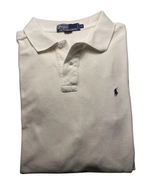 Vit pikétröja från Polo Ralph Lauren - Klassisk vit pikétröja från Polo Ralph Lauren med broderad logga på bröstet. Tröjan har krage, knappar vid halsen och är tillverkad i 100% bomull. Perfekt för en clean och stilren look. Har en litet hål på ryggen kan sy men ett styg och allt är bra 