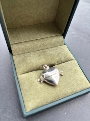 Halsbandshänge i silver från Maria Nilsdotter - Unikt halsbandshänge i form av ett hjärta från Maria Nilsdotter. Hänget är tillverkat i blankt silver och har en modern, geometrisk design med en liten ögla för kedja. Perfekt för dig som gillar stilrena och coola smycken. Kvitto finns. 