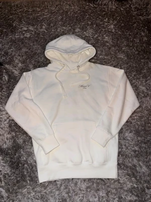 Vit hoodie från Maison V Paris - Snygg vit hoodie från Maison V Paris med broderad logga på bröstet. Hoodien har en stor huva med dragsko, magficka och ribbade muddar vid ärmar och nederkant. Storlek M använd någon ynka gång 