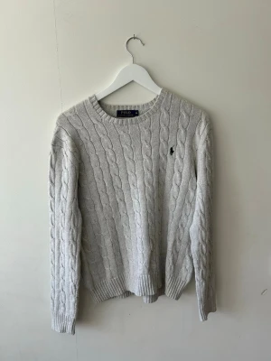 Ljusgrå kabelstickad tröja Polo Ralph Lauren M - Snygg ljusgrå kabelstickad tröja från Polo Ralph Lauren med rund halsringning och klassisk broderad logga på bröstet. Tröjan har ribbade muddar vid ärmslut och nederkant. Tröjan är i storlek Medium😁👍